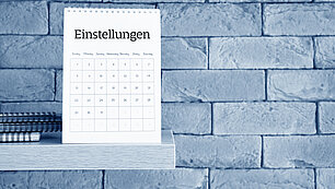 Ein Kalender auf einem Regal vor einer Wand aus Stein